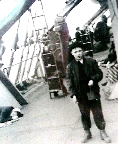 A boy in a suit and cap standing on the deck of a ship, a snapshot from 1951