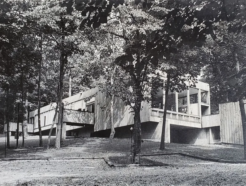 The Schwarzbart home, a modernist house of vertical wood siding raised on concrete piers among tall trees
